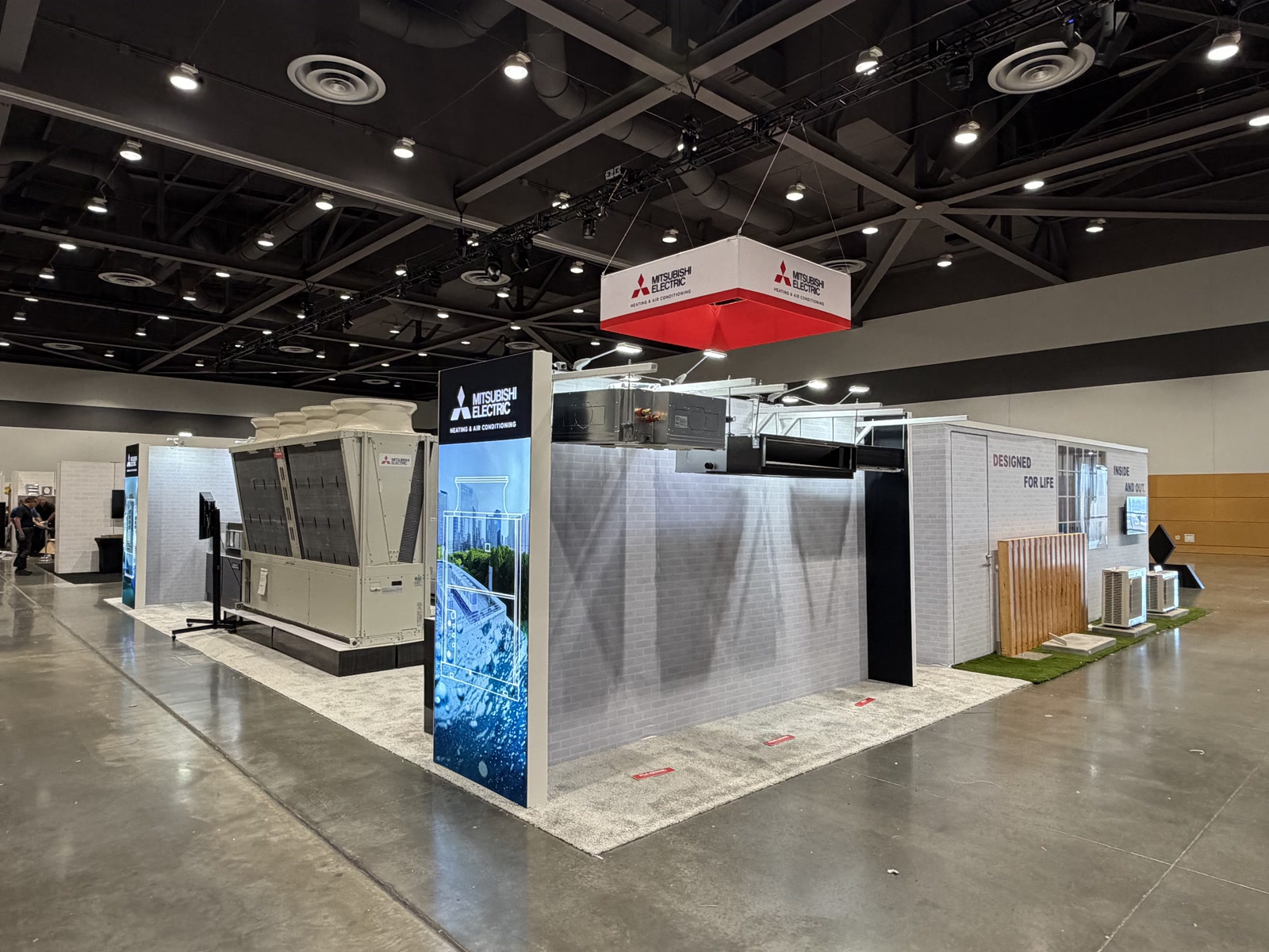 Wide view of the Mitsubishi Electric booth with illuminated hanging brand sign and product display zones.