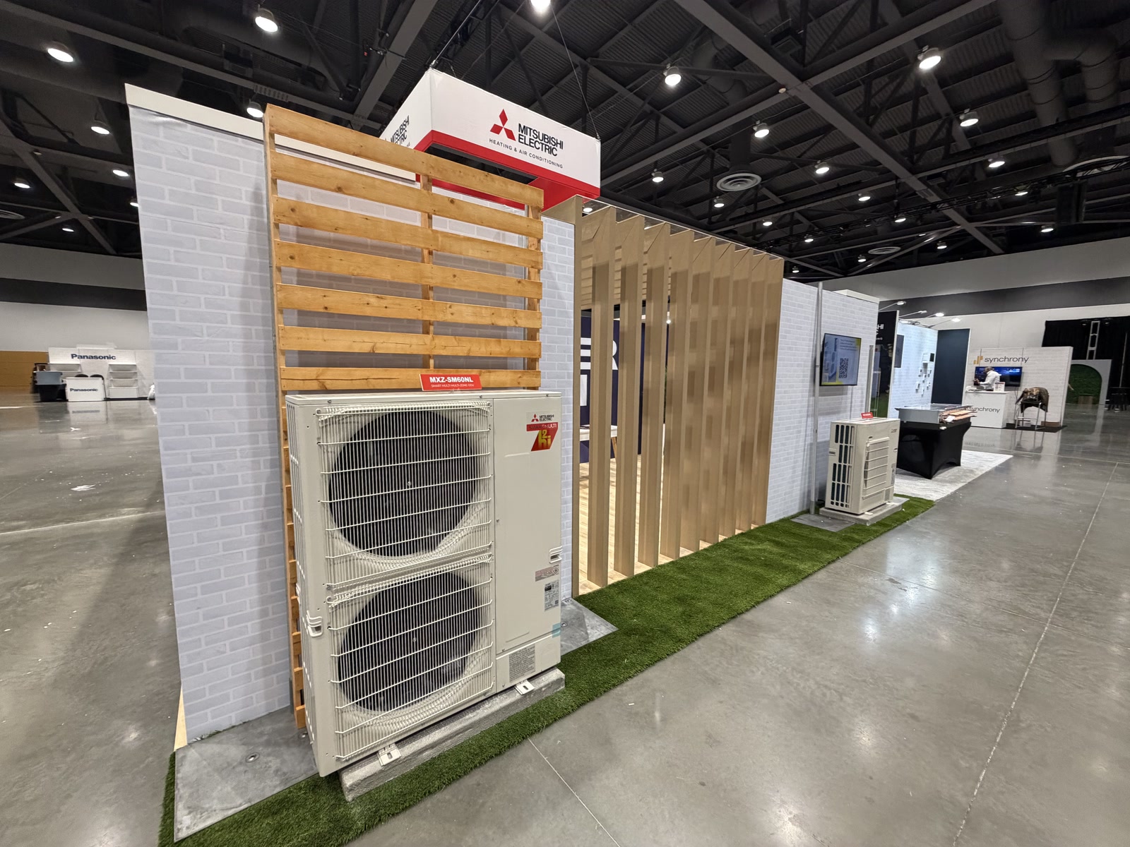 Mitsubishi Electric exterior display structure with outdoor HVAC equipment, turf, and wood slat screening.